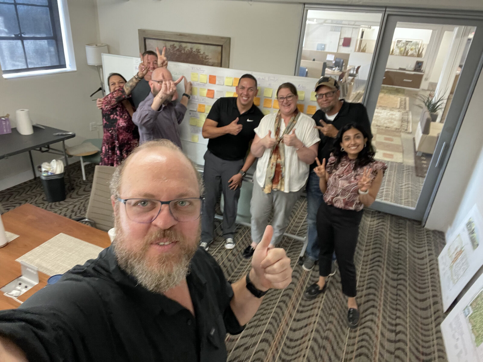 Max with a small business owner's team during a live working session, sticky notes mapping the role on the whiteboard behind them