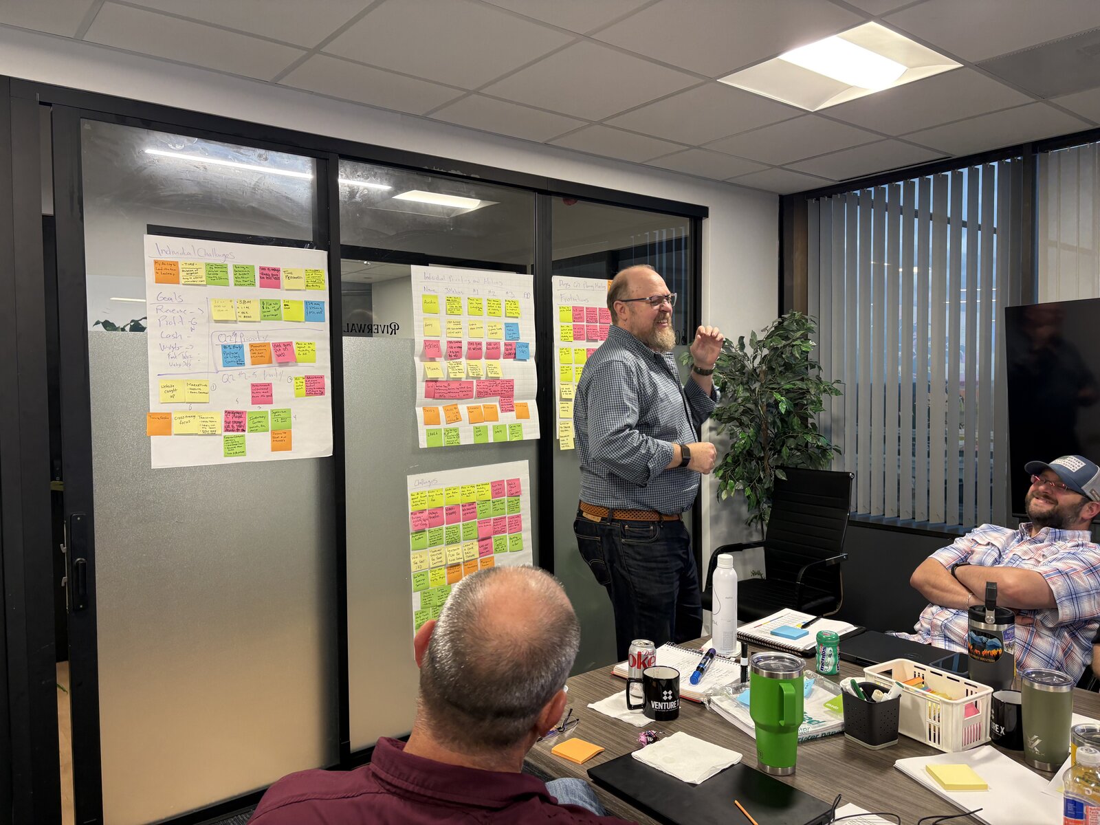 Max facilitating a working session with a small business team, sticky notes mapping the role on the wall behind him